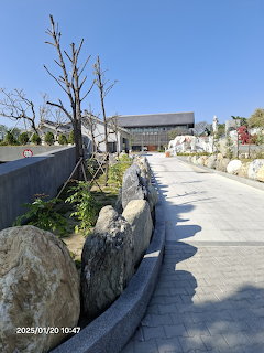 Curved stone-lined walkway with bare trees leading to a modern building under clear blue sky