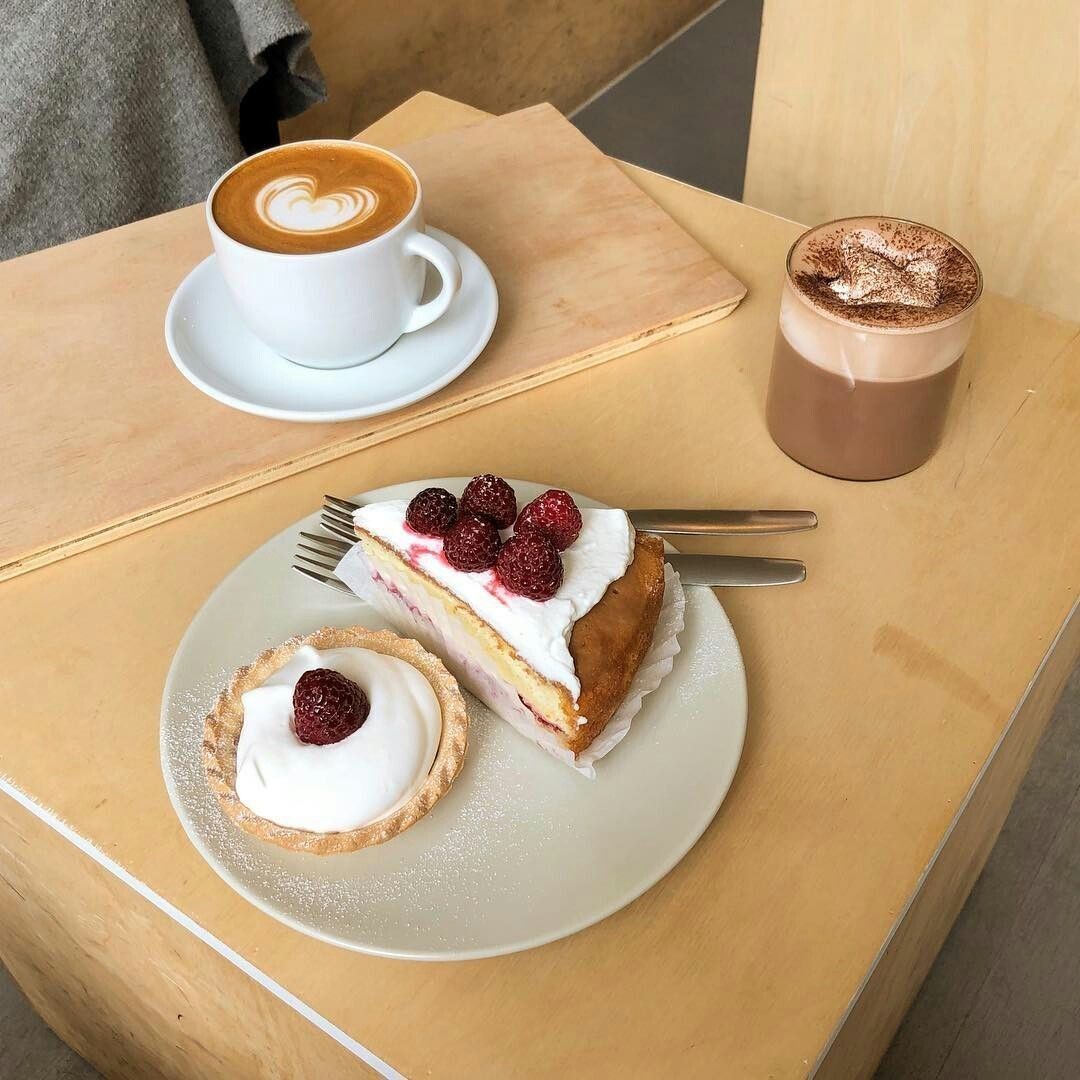 Latte, chocolate drink, and two berry pastries on a wooden café table