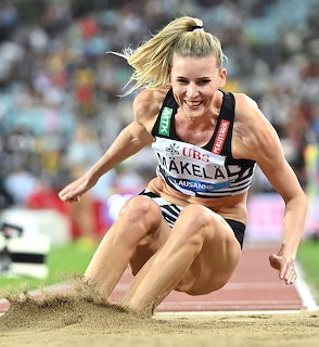 Female athlete mid-flight during long jump landing in sand pit at stadium