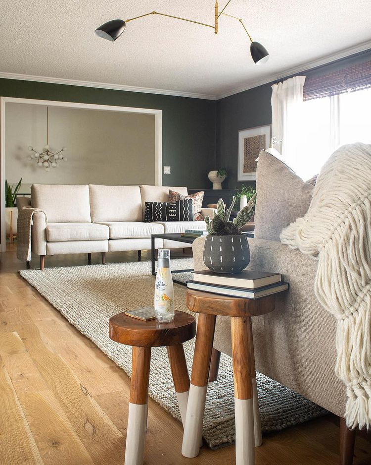 Modern living room with beige sofas, wooden side tables, knit blanket, and dark green walls