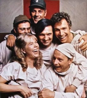 Group portrait of six MASH cast members smiling together in costume