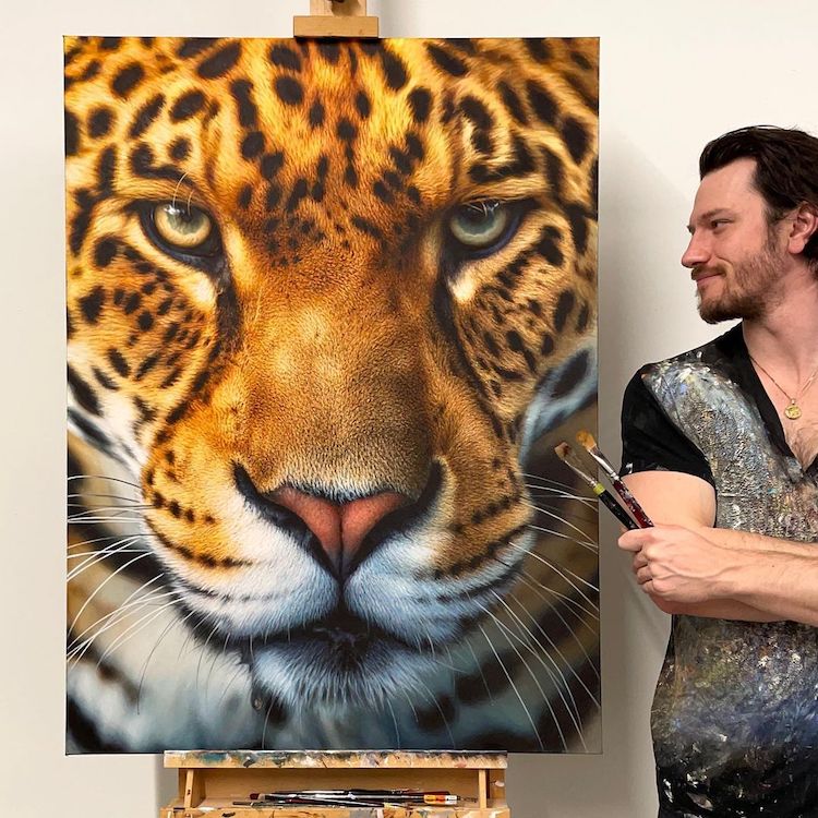 Man holding brushes beside a large tiger face painting on canvas