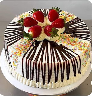 Round cake with white frosting, vertical chocolate drizzle, rainbow sprinkles, and strawberries on top