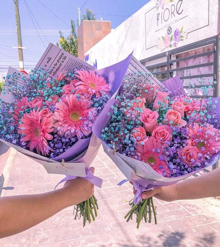 Two hands holding matching pink and purple flower bouquets with roses and daisies outdoors
