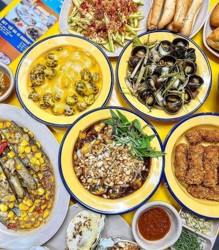 Top-down view of a Vietnamese food spread with multiple plates of snails, corn, and various dishes