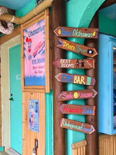 Colorful wooden directional sign pointing to tropical beach destinations beside turquoise building