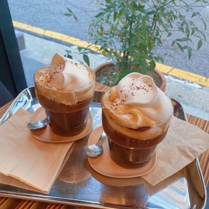Two iced einspanner coffee drinks with whipped cream on a tray by a window