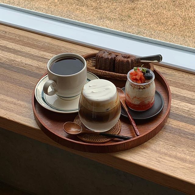 Coffee, iced coffee, and a berry parfait on a round wooden tray by a window