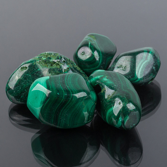 Five polished green malachite stones on a dark reflective surface