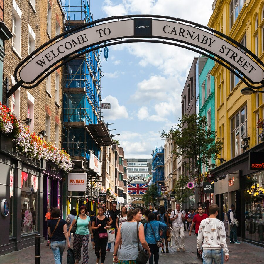 Busy Carnaby Street in London with pedestrians walking under the Welcome to Carnaby Street sign