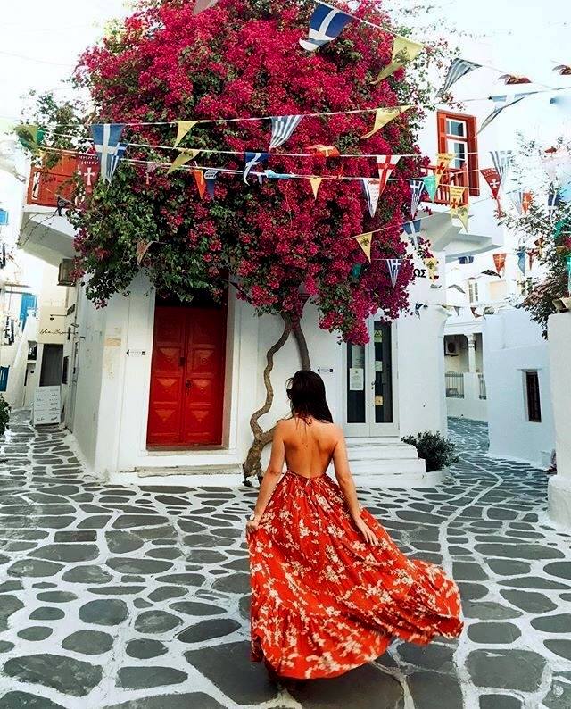 Woman in red dress facing white building with red bougainvillea in Mykonos, Greece