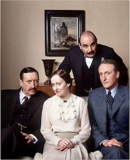 Four people in period costume posed together indoors, one standing behind three seated figures