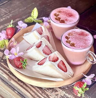 Two pink drinks and strawberry cake slices on a wooden tray with purple flowers