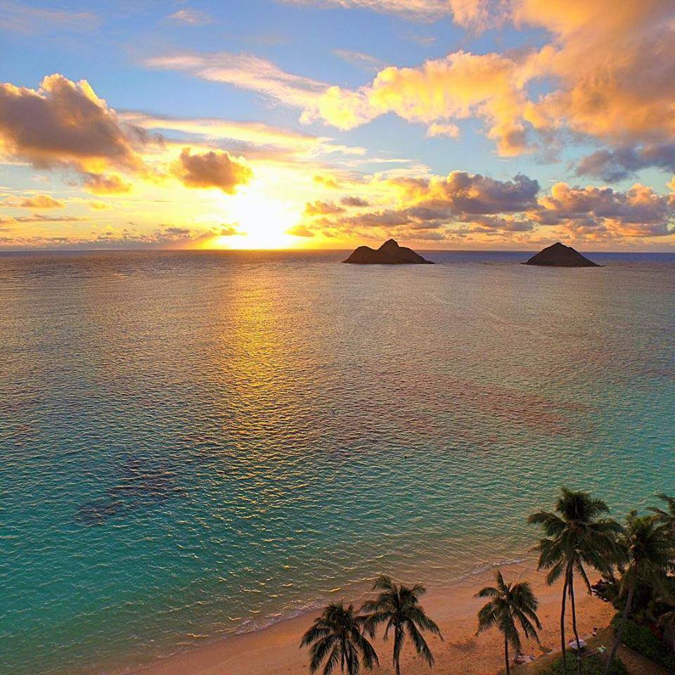 Sunrise over turquoise ocean with palm trees and islands on horizon at Lanikai Beach