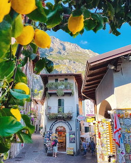 Narrow Italian village street with lemon tree, old buildings with balconies, and mountains in the background