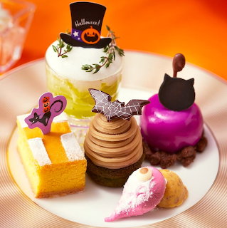 Plate of Halloween desserts with cakes, pastries, and decorative toppers including a black cat and pumpkin design