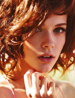 Close-up portrait of a woman with curly reddish-brown hair and green eyes in natural light