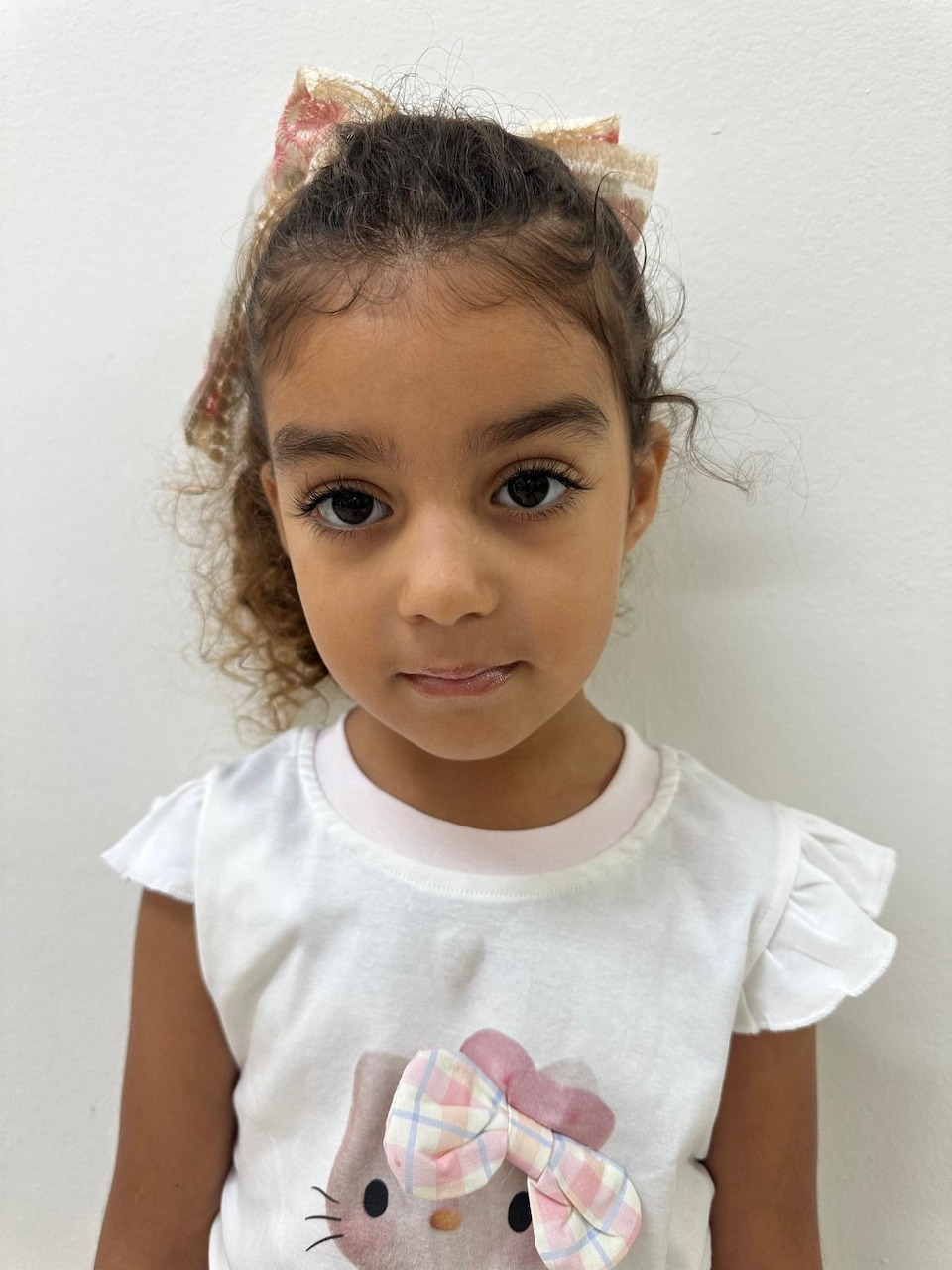 Young girl with curly hair and pink bow wearing a white Hello Kitty shirt