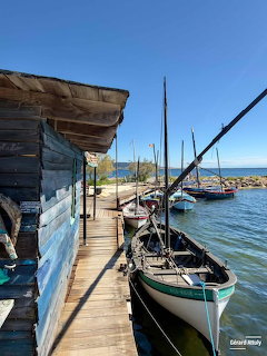 Traditional sailboats docked at a weathered wooden pier beside a rustic shack on a sunny day