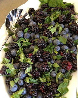 White platter covered with fresh blackberries, blueberries, and green mint leaves with two spoons