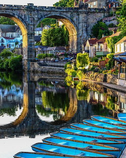 Stone viaduct over the River Nidd in Knaresborough with riverside houses, reflections, and blue boats