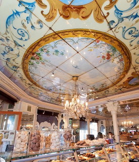 Interior of an ornate Parisian bakery with painted ceiling, chandelier, and pastry displays