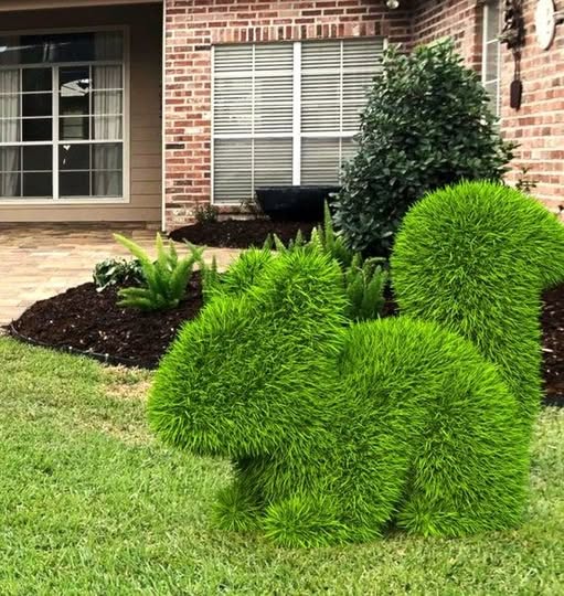 Green grass dinosaur topiaries on a residential front lawn with brick house in background