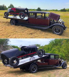 Burgundy vintage hot rod truck with black classic speedster on flatbed in rural setting