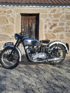 Blue vintage Triumph T100 motorcycle parked against stone building wall