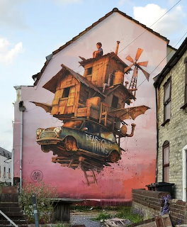 Colorful mural on building wall showing surreal flying wooden house with windmill and vintage car against pink sunset sky