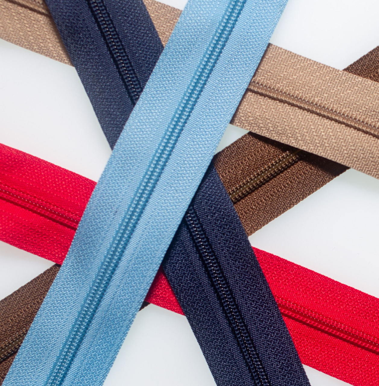 Close-up of red, blue, brown, and beige zippers crossing on a white background