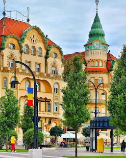 Colorful Art Nouveau buildings with green domed tower and Romanian flag in Oradea city square