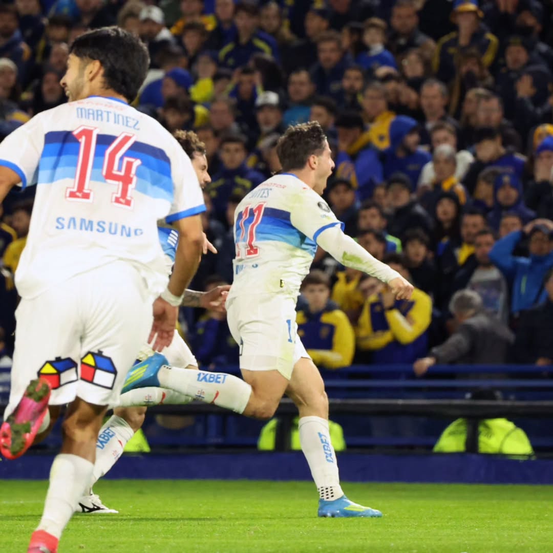 Soccer players celebrating a goal during a night match with crowd in stadium background