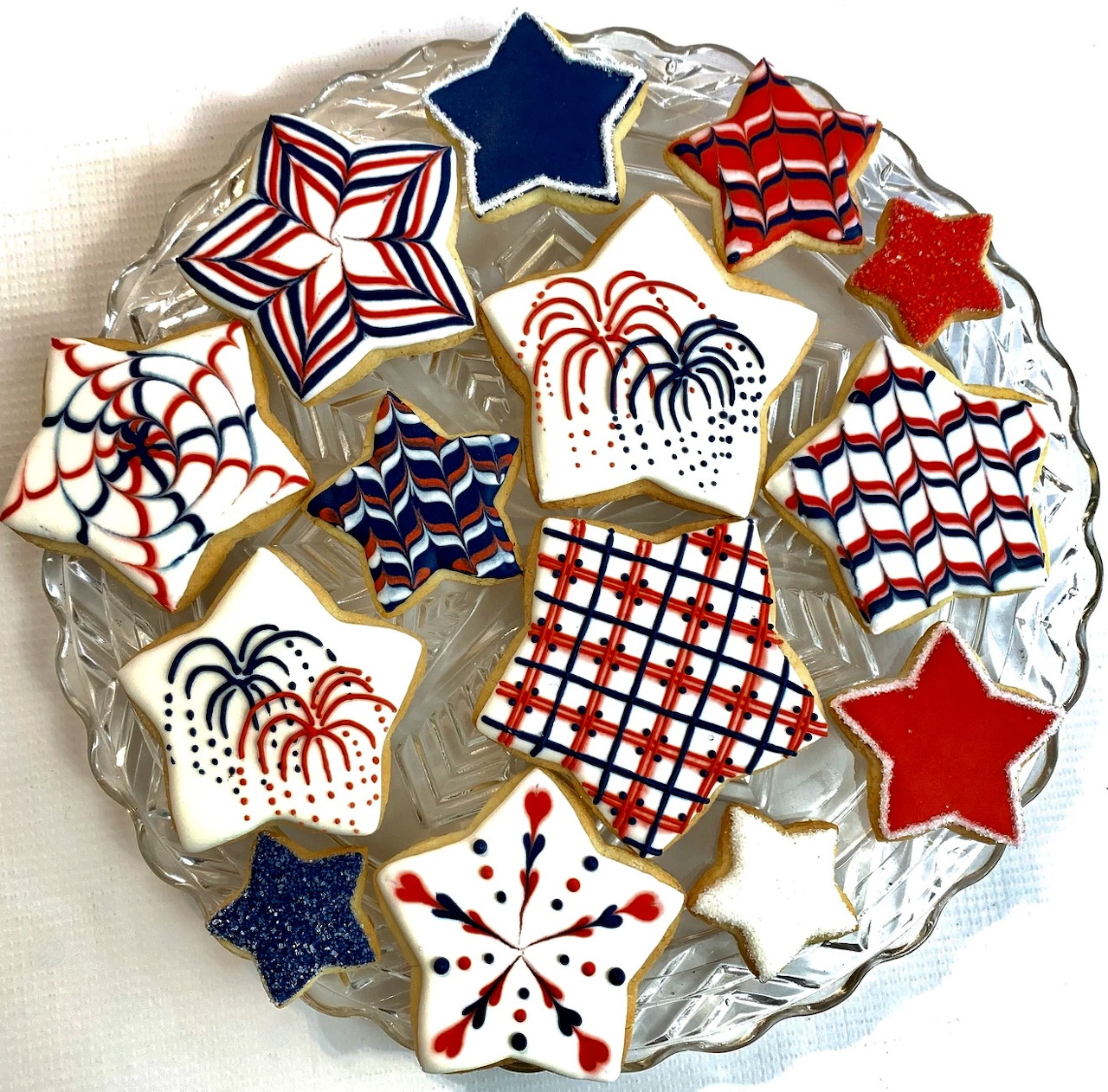 Star-shaped cookies on a glass plate decorated with red, white, and blue icing in patriotic patterns