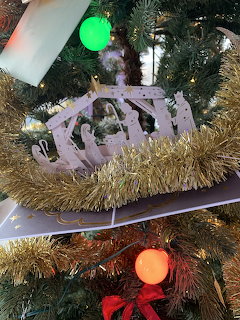 Metal nativity scene ornament on a Christmas tree with gold tinsel and colorful lights