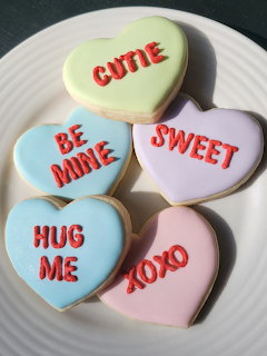 Five pastel heart-shaped cookies with Valentine messages arranged on a white ridged plate
