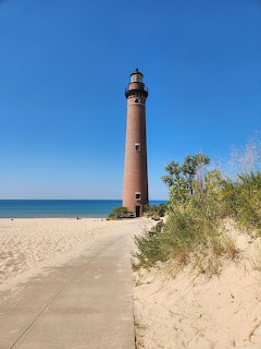Tall red brick lighthouse on sandy beach with dunes and clear blue sky
