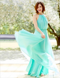 Woman in flowing turquoise chiffon dress posing outdoors with fabric blowing in the wind