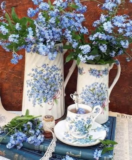 Vintage floral pitchers with blue forget-me-nots, matching teacup on blue books with lace doily
