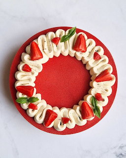 Top view of a strawberry cake with whipped cream swirls and fresh strawberry halves on a red plate