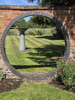Circular brick arch opening in garden wall revealing lawn, white planters and trees