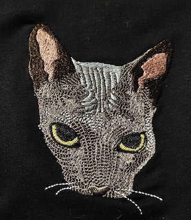 Gray embroidered cat face with green eyes on black fabric