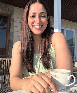 Smiling woman holding a white tea cup while sitting outdoors in sunlight