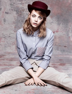 Young woman in burgundy hat and blue shirt sitting cross-legged against a grey backdrop