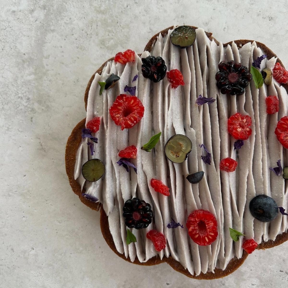 Flower-shaped pastry with white glaze, berries, and mint leaves on marble surface