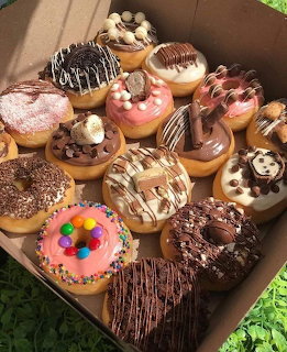 Open box containing assorted decorated donuts with various frostings and toppings