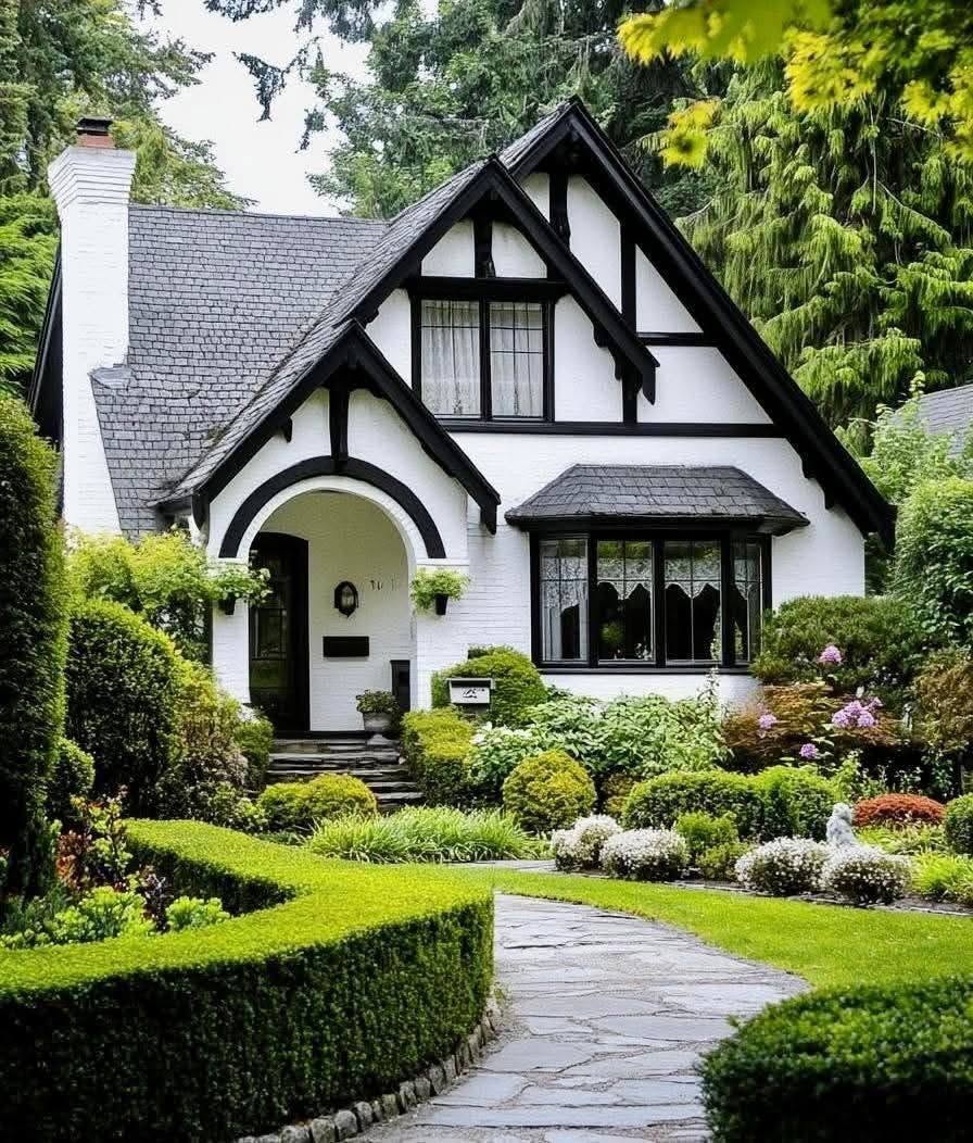 Black and white Tudor-style house with manicured hedges, shrubs, and a curved stone garden path