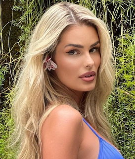 Portrait of blonde woman in blue top outdoors with green foliage background