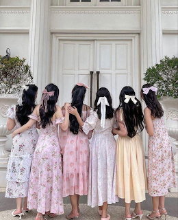 Six girls in pastel dresses seen from behind with hair bows standing in front of white doors