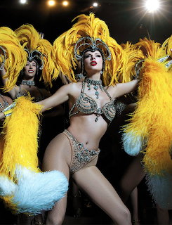 Showgirl in jeweled costume with yellow and blue feather fans and tall feathered headdress performing on stage